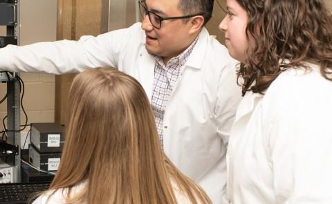 Three UNE researchers examine a microscope